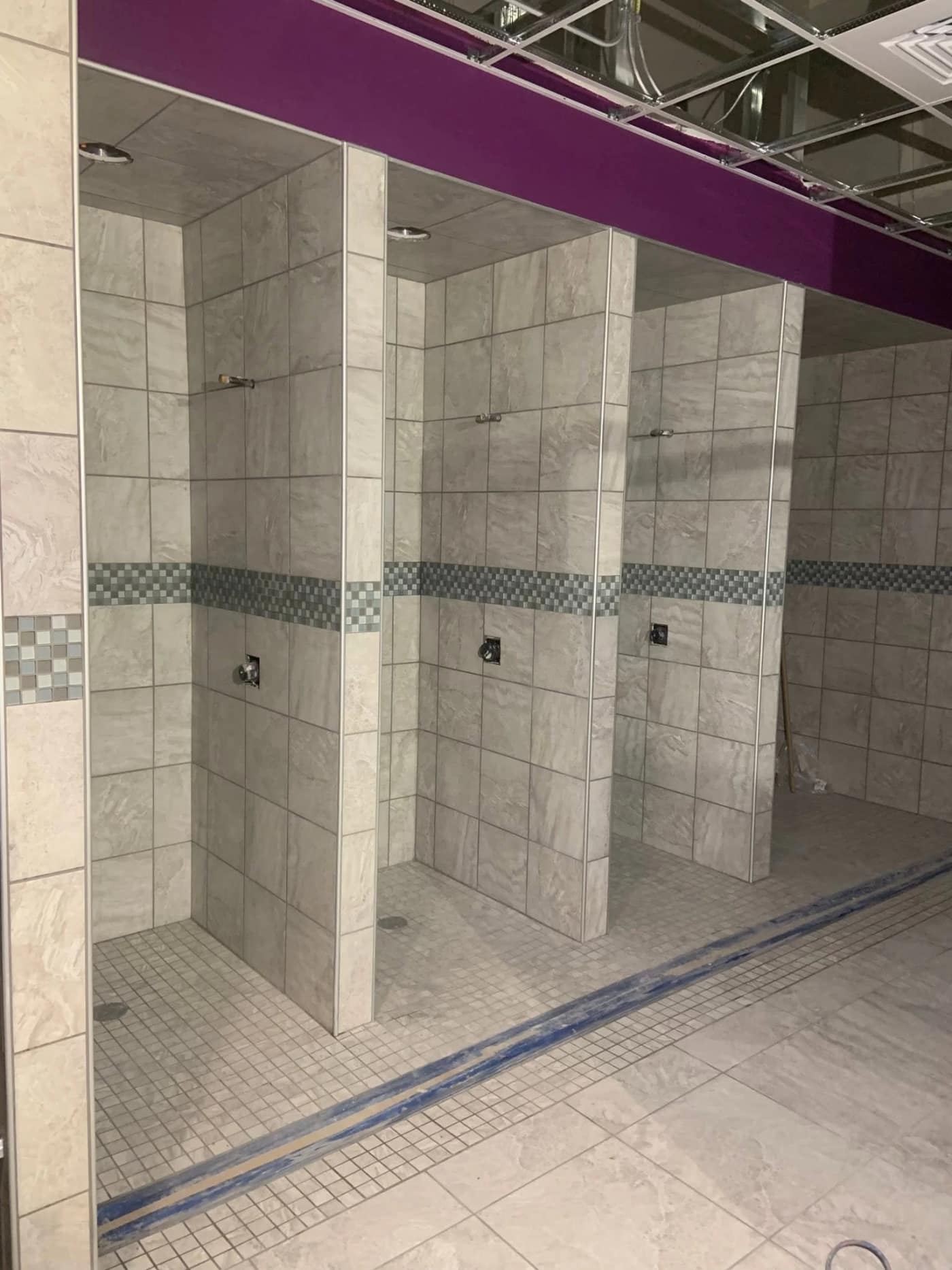A row of tiled locker-room shower stalls with a checkerboard mosaic band at Planet Fitness