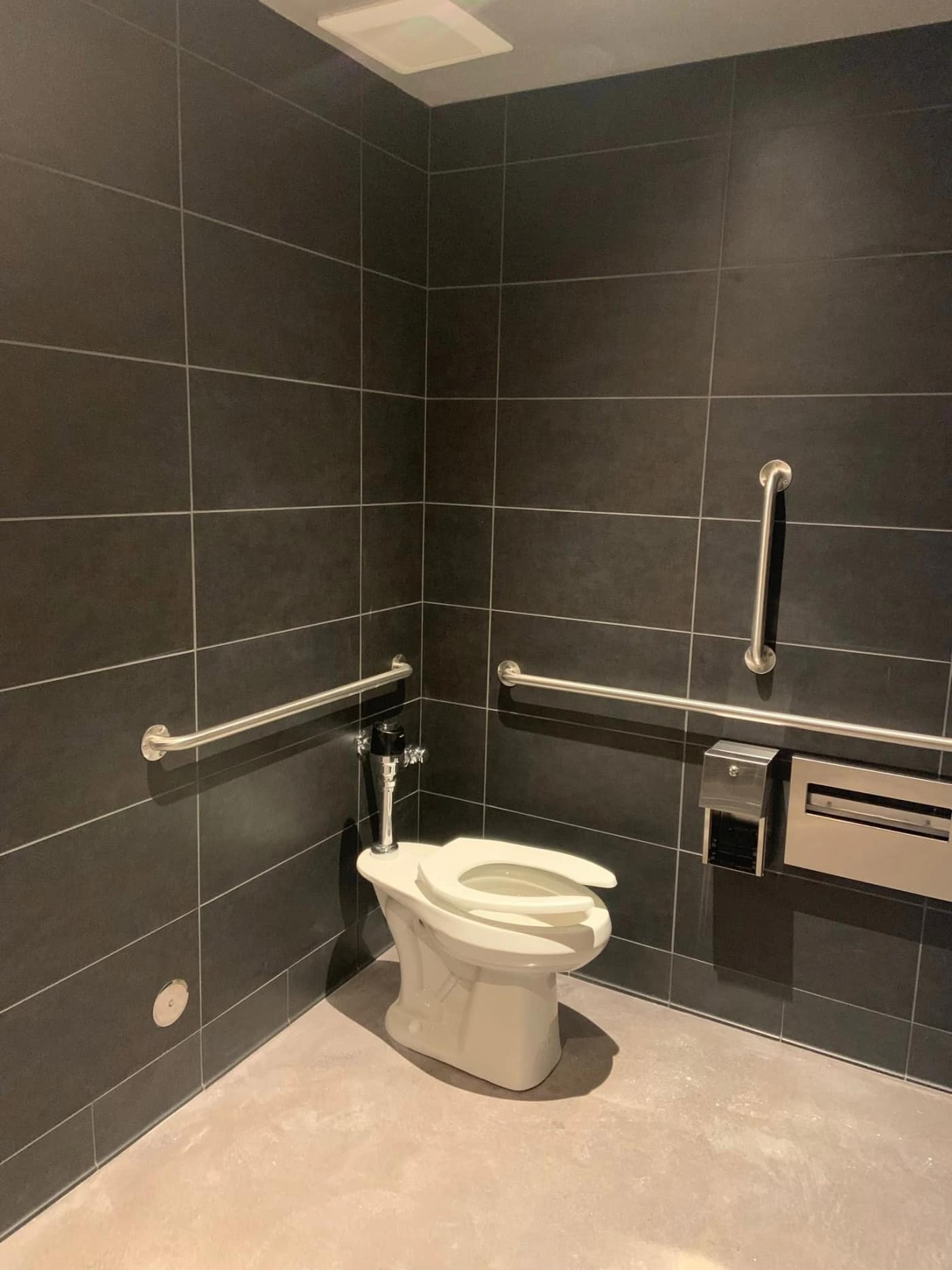A Starbucks restroom in dark charcoal large-format tile with grab bars