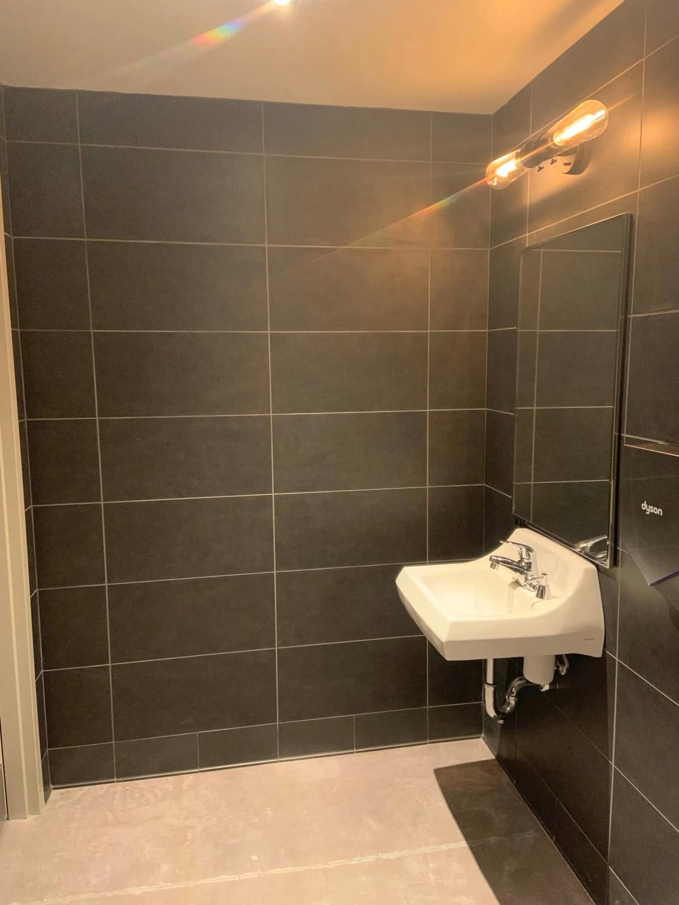 A Starbucks restroom in charcoal large-format tile with a warm sconce